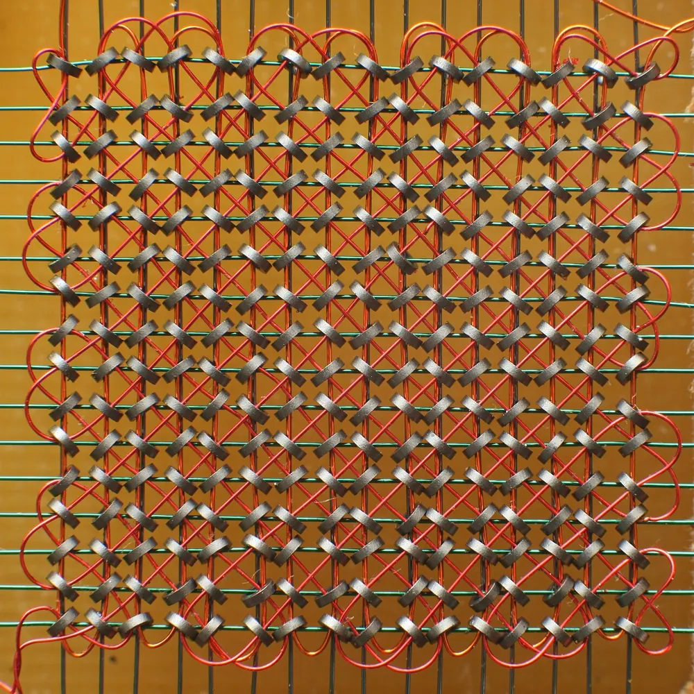 Macro photograph of a magnetic core memory plane: tiny ferrite rings threaded on a grid of fine wires.